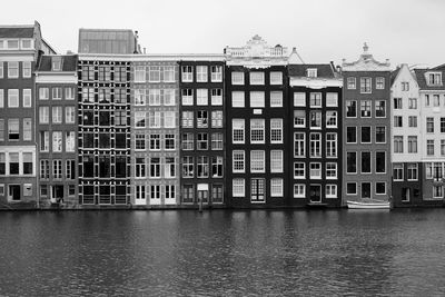 Houses by river in city against sky