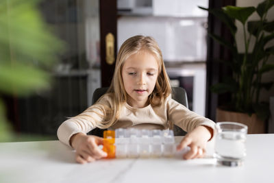 Cute girl with medicine container sitting at table