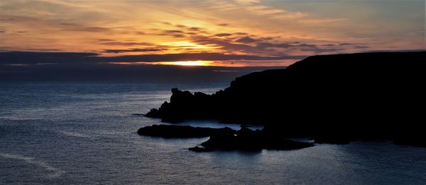 Silhouette rocks on sea against sky during sunset