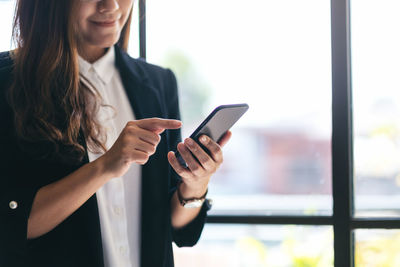 Young woman using mobile phone while standing on window