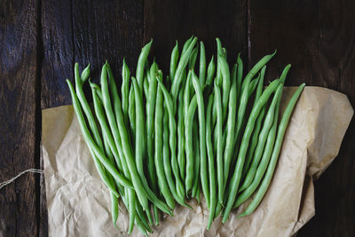 High angle view of green beans with wax paper on wooden table