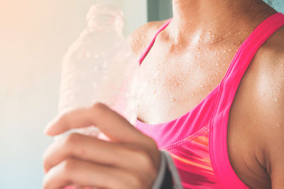 Midsection of woman with water bottle standing against wall