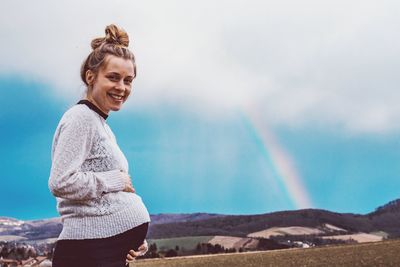 Young woman smiling while standing on mountain against sky