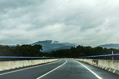 Empty road by mountains against cloudy sky