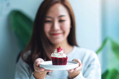 A beautiful asian woman holding a plate of red velvet cup cake