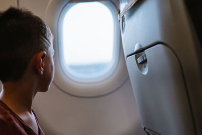Side view of calm boy sitting on chair looking out the windows in plane