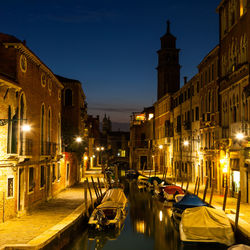 Boats moored in canal amidst buildings in city at night