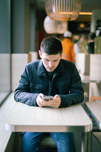 A young man with a phone in his hands is sitting in a diner.