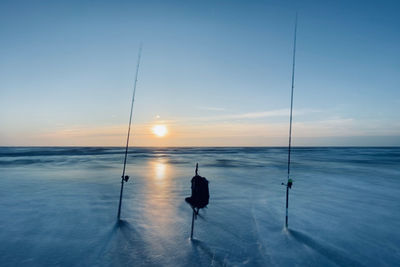 Silhouette fishing rod on sea against sky at sunset in longtime exposure