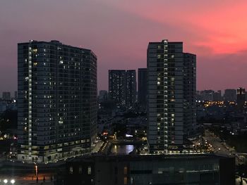 Illuminated buildings in city against sky at dusk