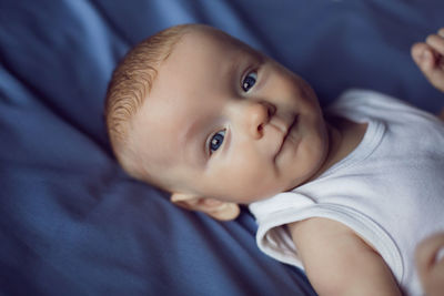 Baby boy blonde in white bodysuit lying on the bed