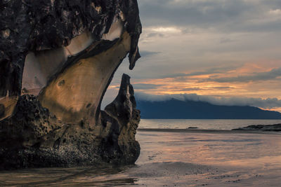 Rock formation on beach against sky during sunset