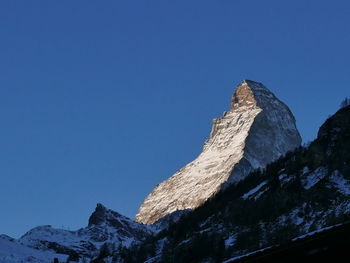 Low angle view of snowcapped mountain against clear blue sky