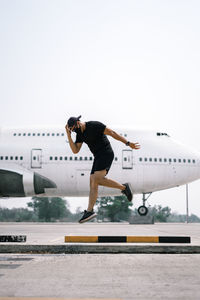 Full length of man jumping against airplane