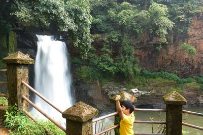 Boy standing by waterfall in forest