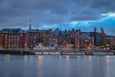 Buildings by river against sky