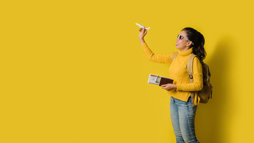 Woman holding umbrella standing against yellow background