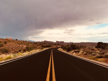 Empty road amidst field against cloudy sky during sunset