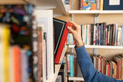 Woman hand picking book from bookshelf in library in university, college, high school or bookshop