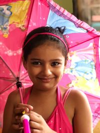 Portrait of smiling girl holding pink umbrella while standing outdoors