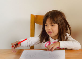 Girl looking away while drawing palms on white paper against wall