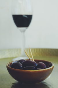 Close-up of black olives in bowl against wineglass on table