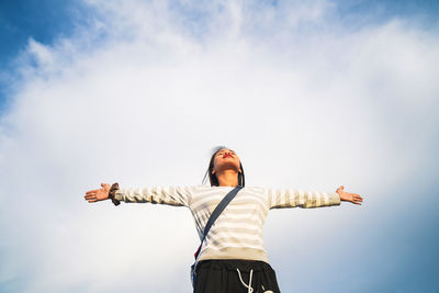 Low angle view of woman with arms outstretched standing against sky