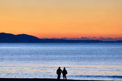 Rear view of people walking at beach against moody clear sky during sunrise