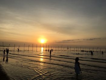 Silhouette people standing on beach against sky during sunset