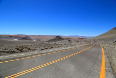 Road amidst desert against clear blue sky