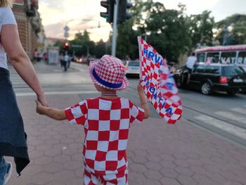 Rear view of boy carrying croatian flag while walking with mother in city