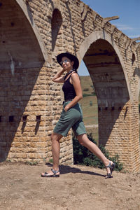 Woman traveler explorer in a black hat walks next to the destroyed old stone bridge in the summer