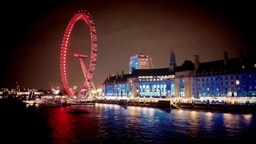 Illuminated ferris wheel by river at night