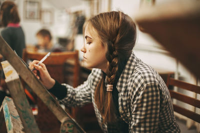 Beautiful teenage girl at art school painting on easel, art studio