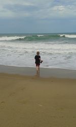 Rear view of woman standing on beach against sky