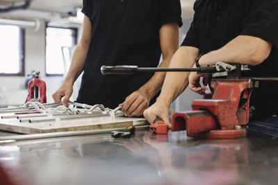 Midsection of auto mechanic teacher and student working at workbench