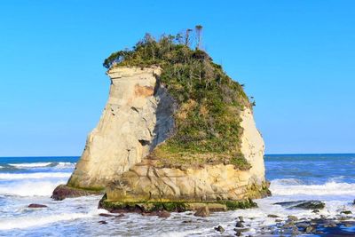 Rock formation by sea against clear blue sky