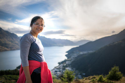 Portrait of smiling woman standing on hill against lake at queenstown