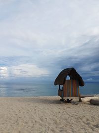 Hut at beach against cloudy sky