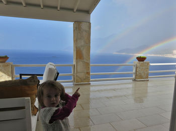 Portrait of cute girl pointing at double rainbow against sea