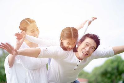 Mother and smiling girl with arms raised against clear sky