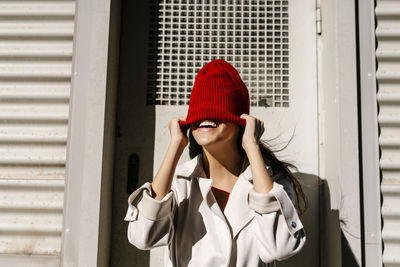 Woman hiding face with knit hat in front of door