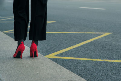 Low section of woman in red high heels standing at sidewalk