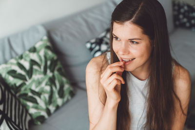 Young woman looking away while sitting on sofa at home