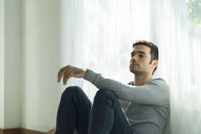 Depressed man sitting by curtain at home