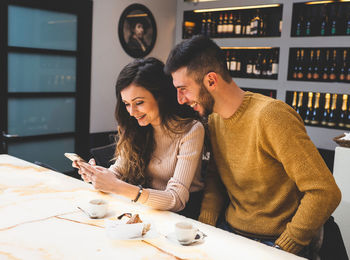 Smiling couple using phone while siting in cafe