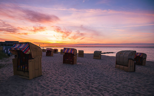 Hooded chairs on beach against sky during sunset