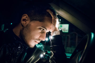 Young man with illuminated string light sitting in car at night