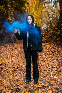 Young woman holding distress flare while standing in forest during autumn