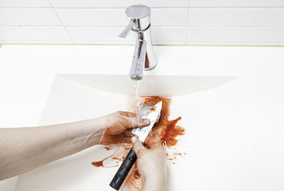 Close-up of hand cleaning knife covered in blood at bathroom